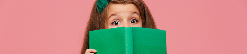 Une petite fille avec les yeux écarquillés qui tient un livre ouvert devant elle